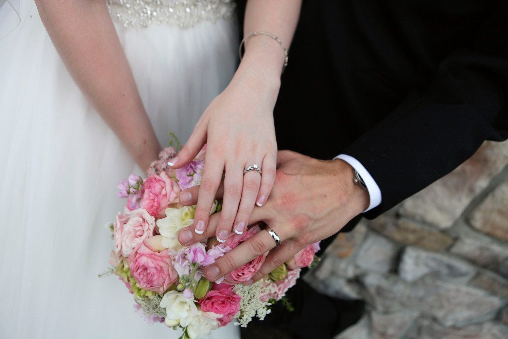 Bride and groom show rings over summer wedding flowers