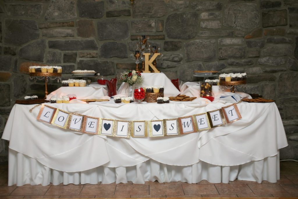 creative wedding favor idea of decorated table of cookies and homemade treats. banner is attached to front of table displaying "love is sweet"