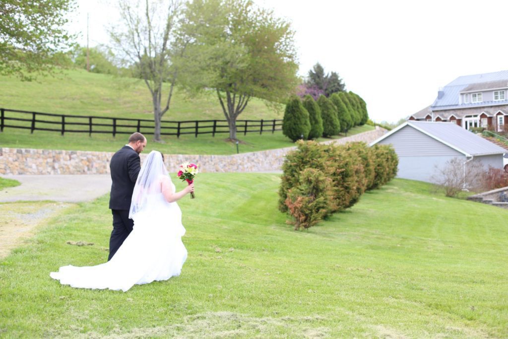 Outside wedding at Morningside Inn, bride and groom pose with rolling hills, wooden fence and country inn as backdrop