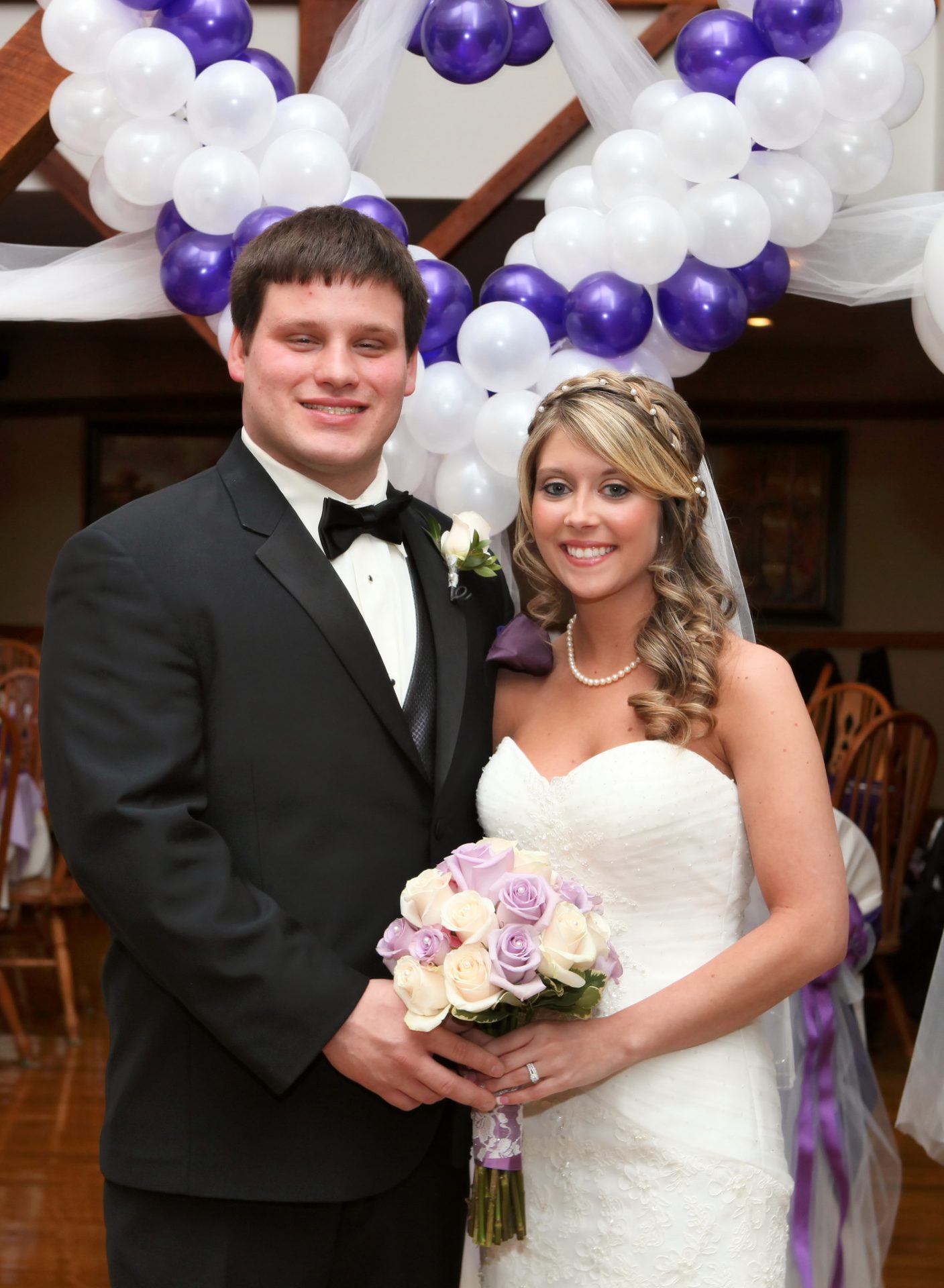 Bride and groom pose in front of white and lavander ballons