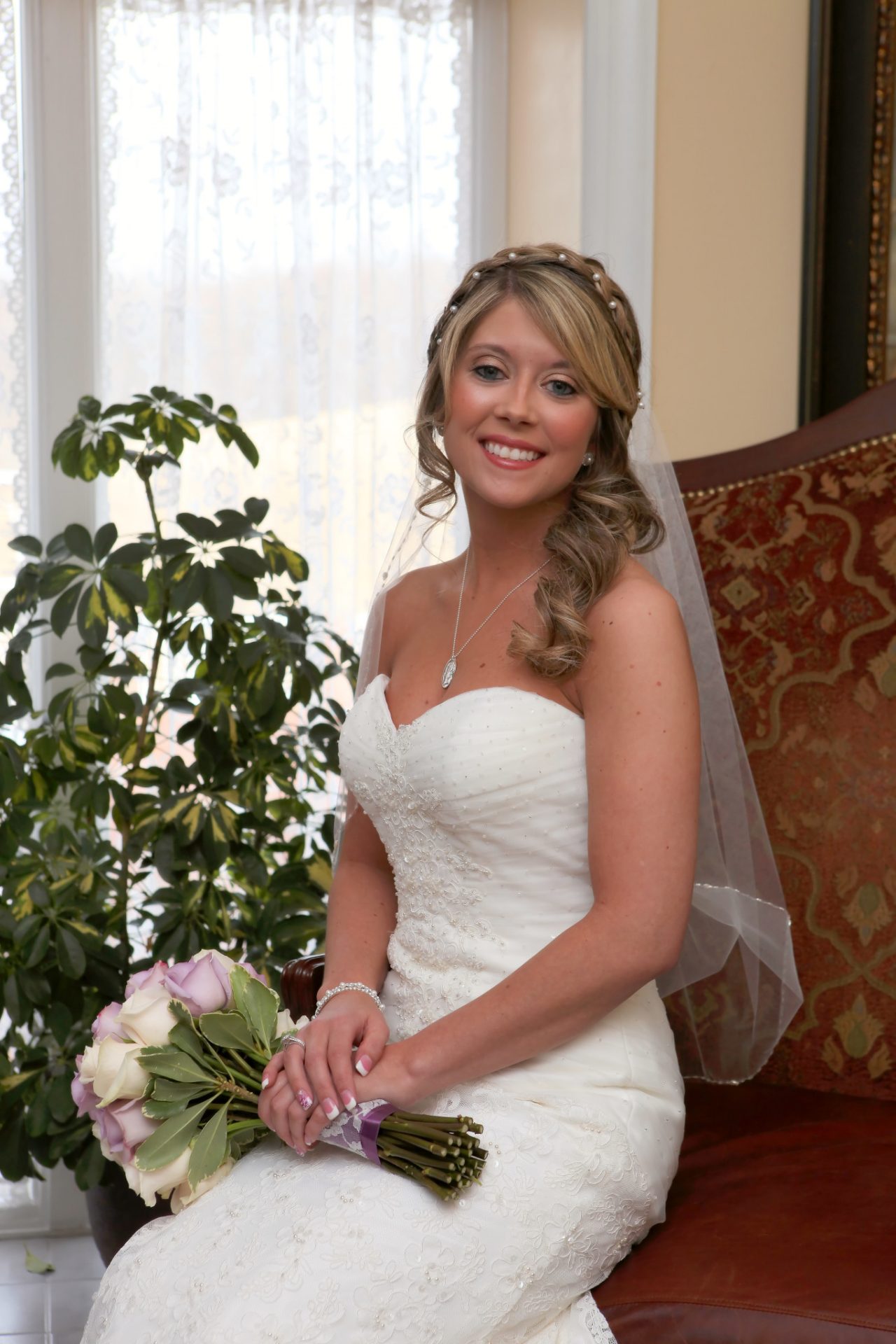 Bride sitting on leather couch by window in bride's room before wedding ceremony