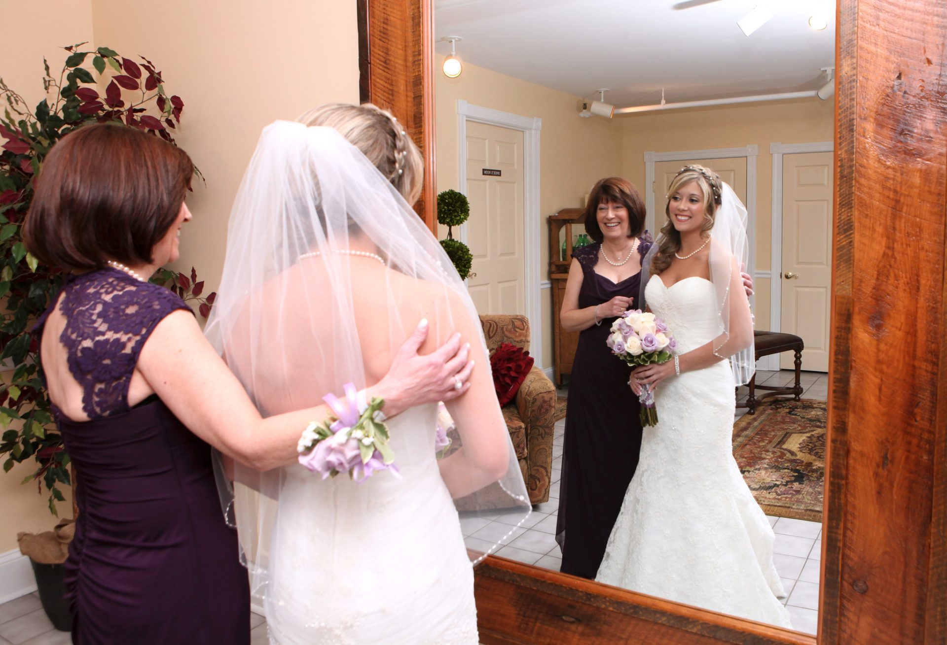 Bride and mother of bride embrace in front of large mirror in the bride's room