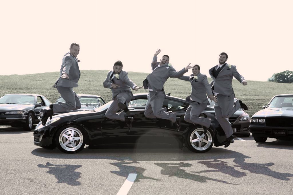 groomsmen jumping by car in parking lot