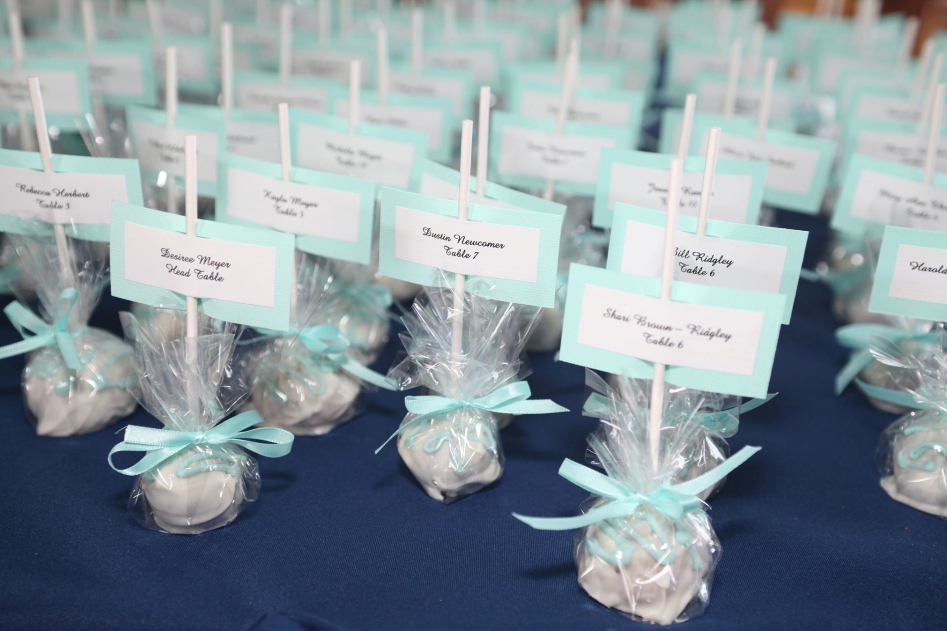Cake pop party favors wrapped in plastic with teal bow also used as table assignments