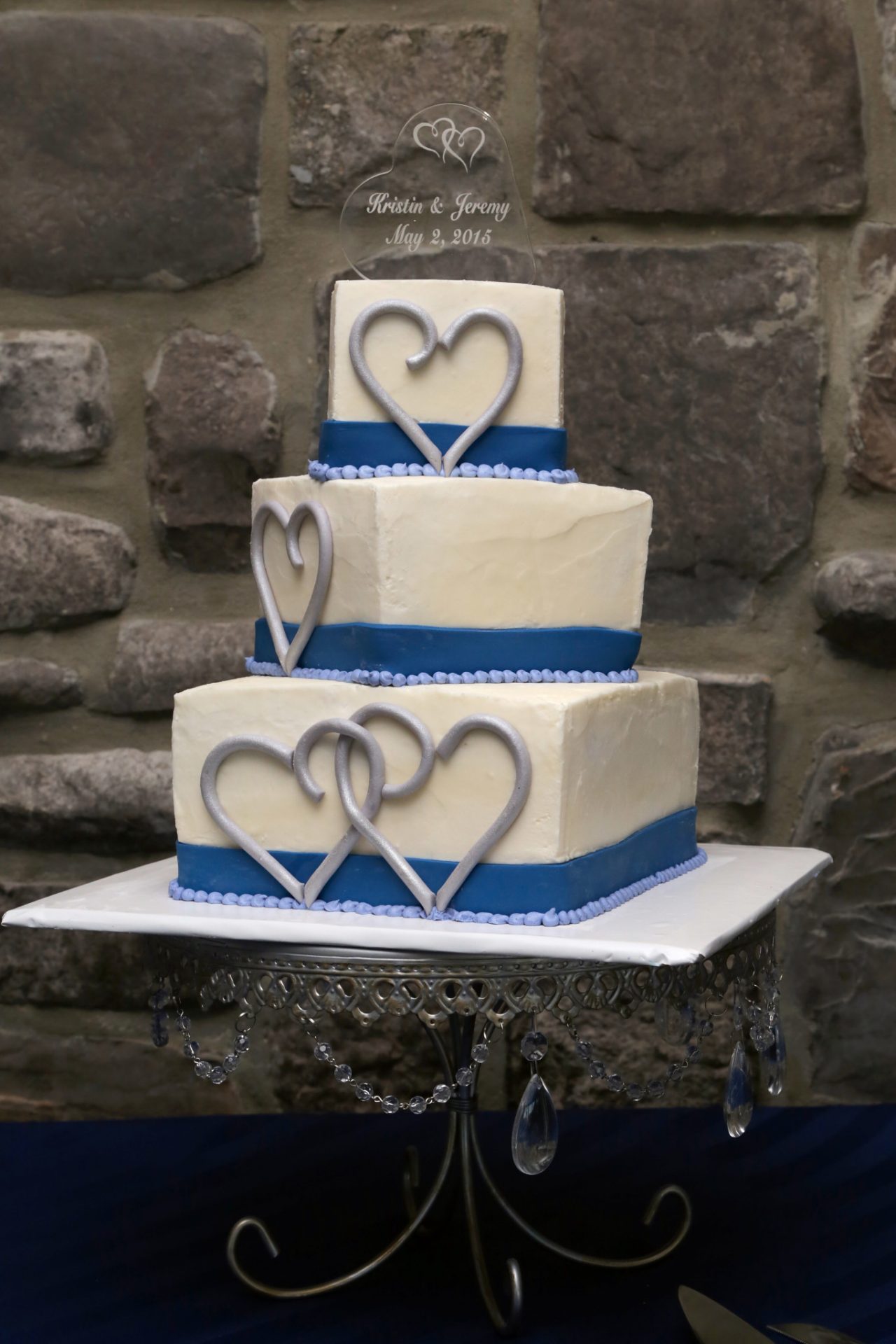 Jeremy and Kristin's cream and blue wedding cake with silver hearts drawn in icing on the sides of three tiered cake