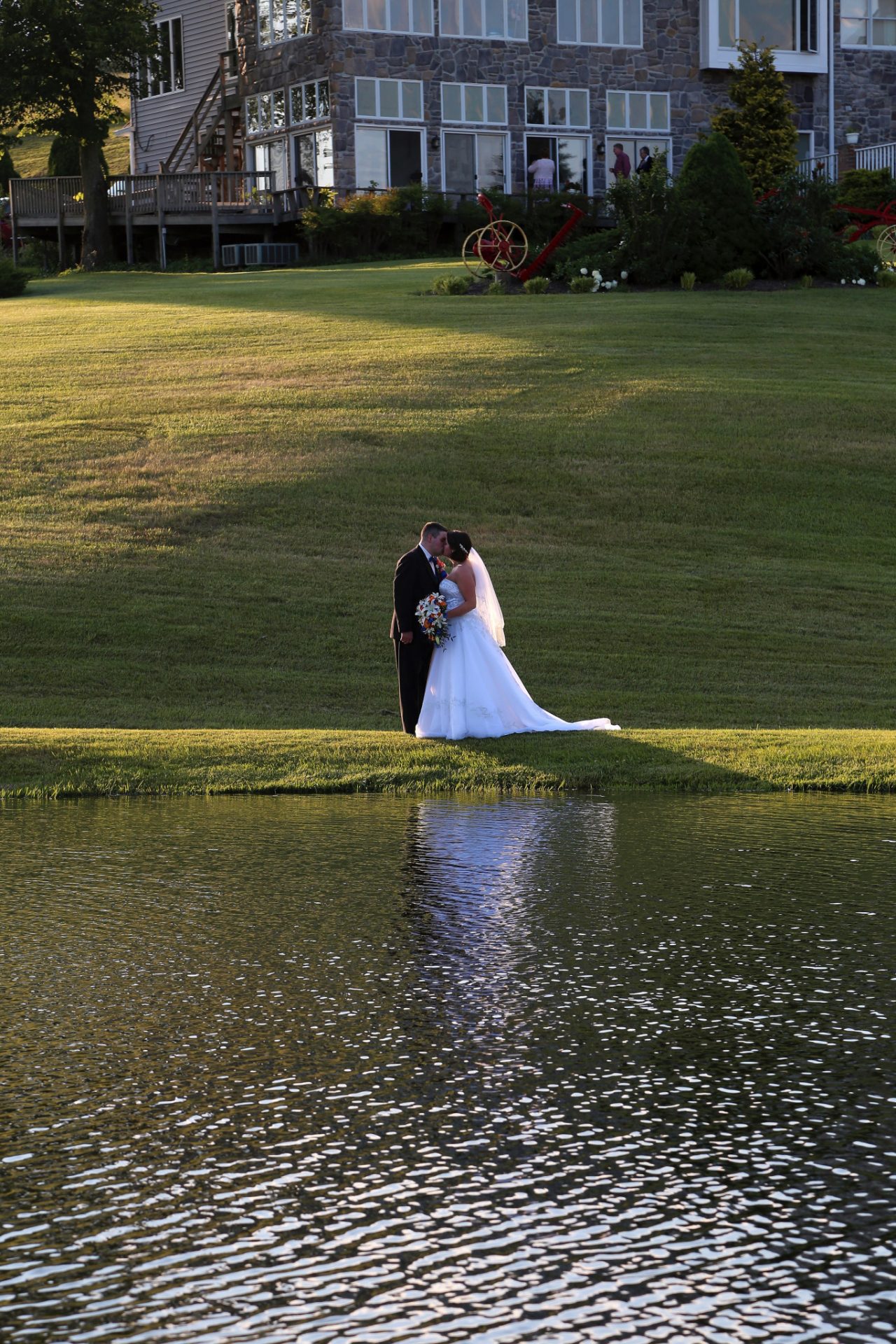 bride and groom pose for photos in front of the pond wedding