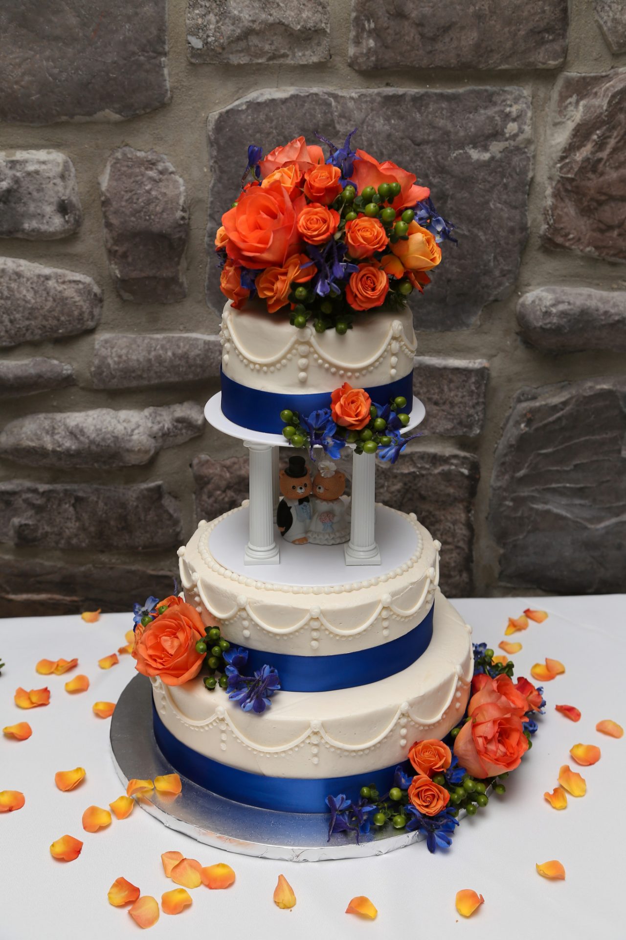 wedding cake with cream icing and pink, orange flowers and blue ribbon