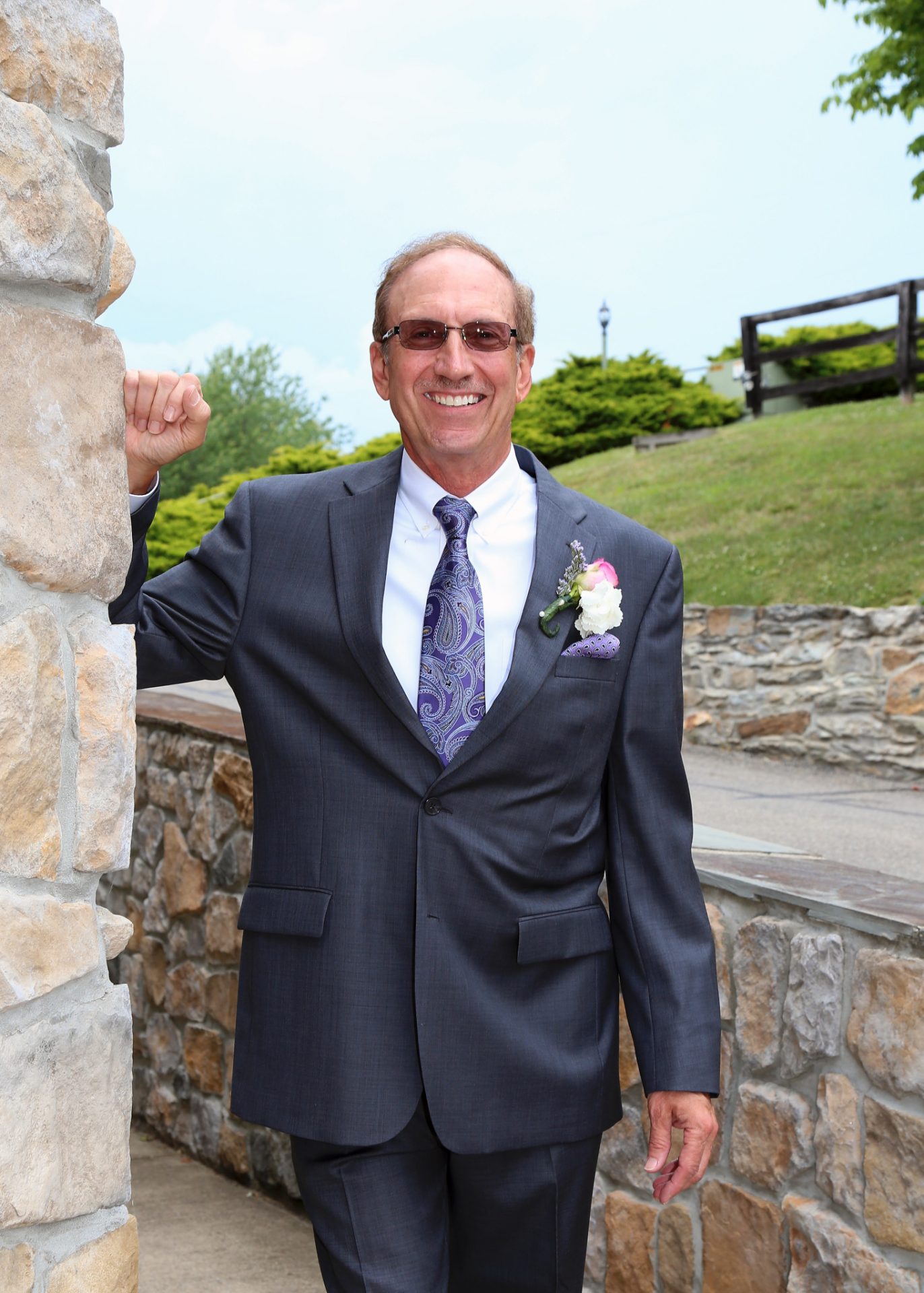 Groom poses by the stone wall in the back of Morningside In before the wedding ceremony on the outdoor pavilion