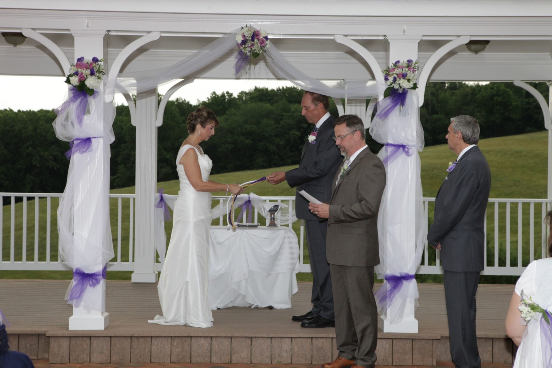 Summer wedding at Morningside Inn on the outdoor pavilion. Bride and groom hold hands on the pavilion decorated with purple and pink flowers and white linen
