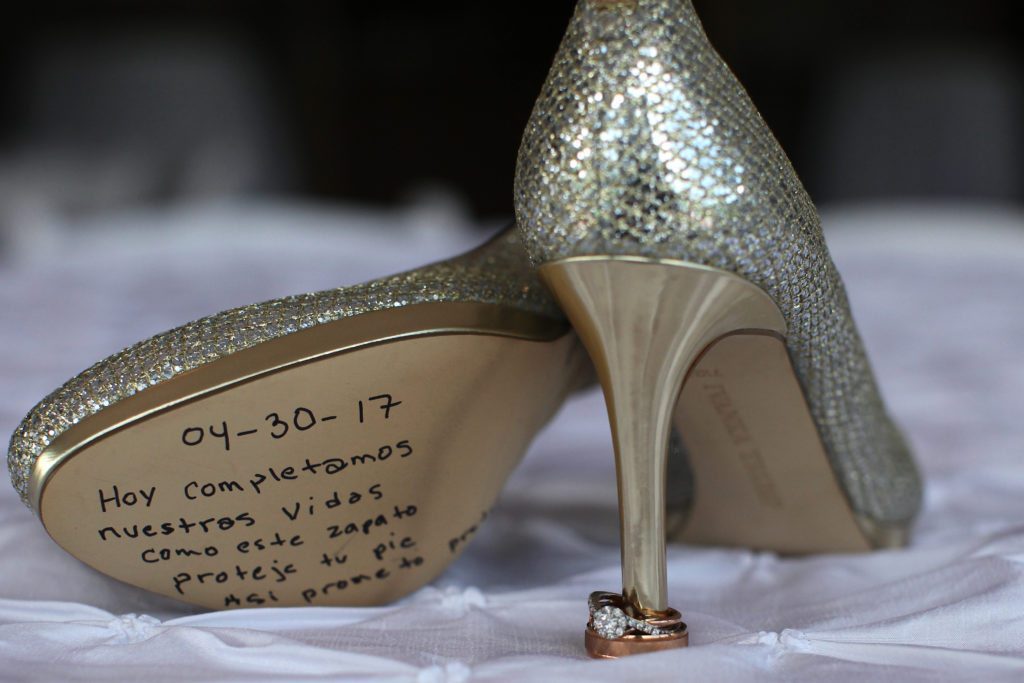 Close-up of a pair of silver high heels with a handwritten message in Spanish on the bottom of the left shoe from Gaby & Victor's Wedding. The message reads, "04-30-17 Hoy completamos nuestras vidas como este zapato Proteje tu pie así como yo protejo tu vida." Two rings rest at the heel. | Morningside Inn