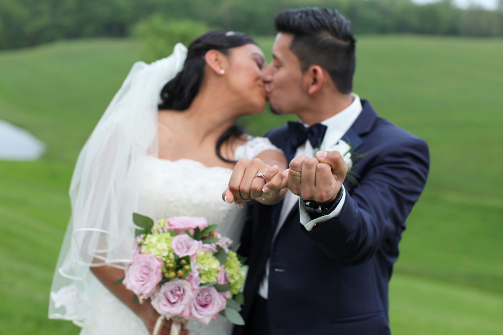 Bride and groom show rings while kissing in back field of Morningside Inn wedding venue in Frederick MD