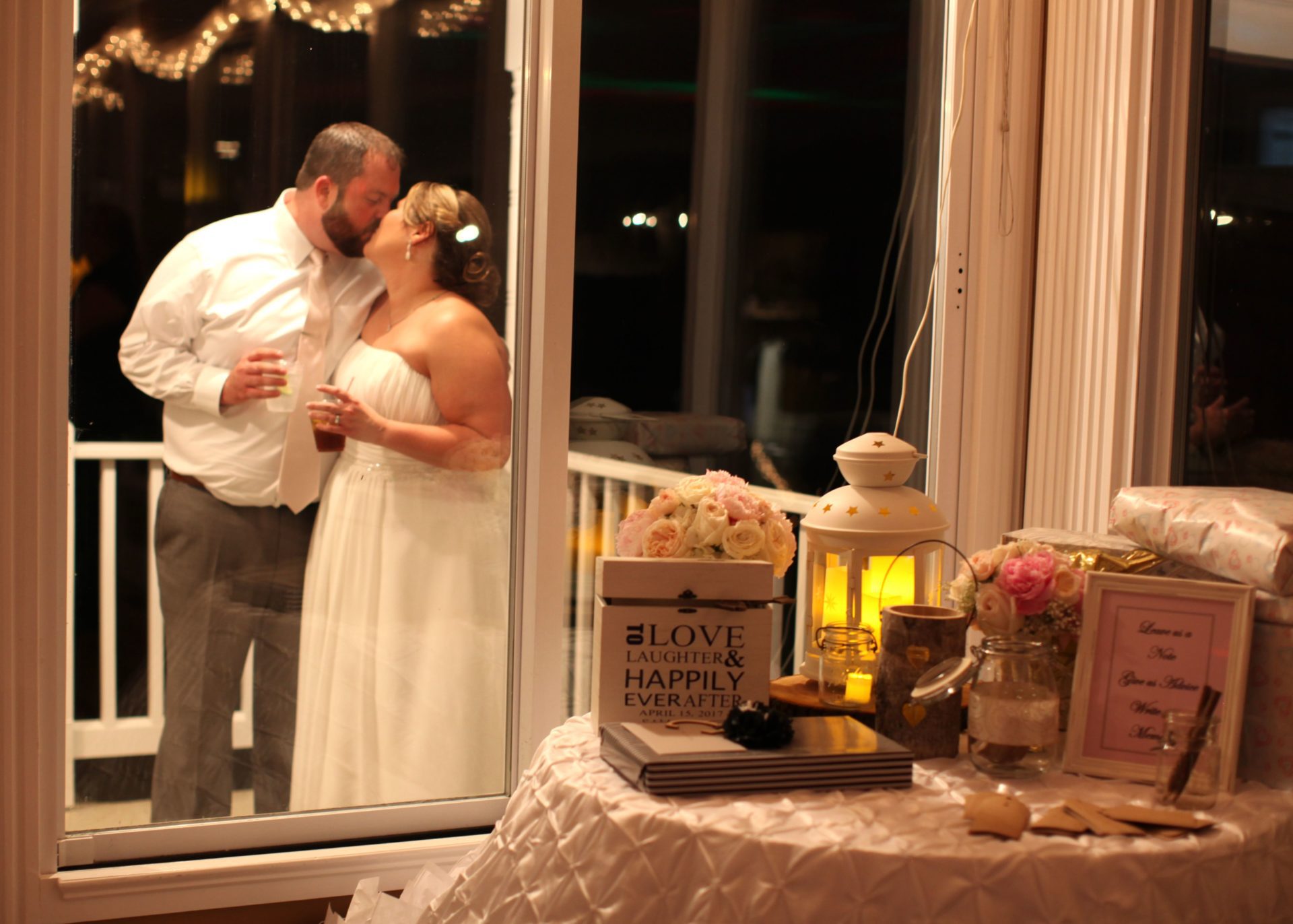 Bride and groom kiss outside reception room window 