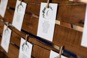 Alt text: Seating assignment cards with names and table numbers hung on a rustic wooden frame with clothespins. The card for table number 6 is in focus.