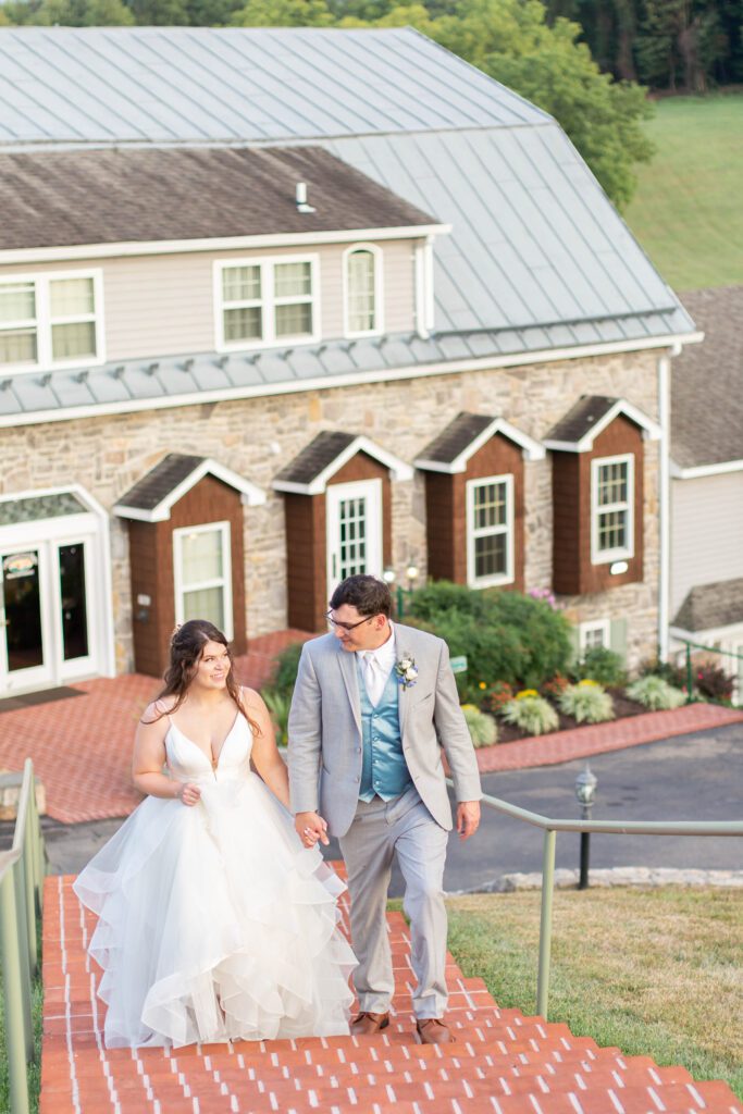 A bride and groom holding hands and walking down a brick pathway with a stone building in the background.