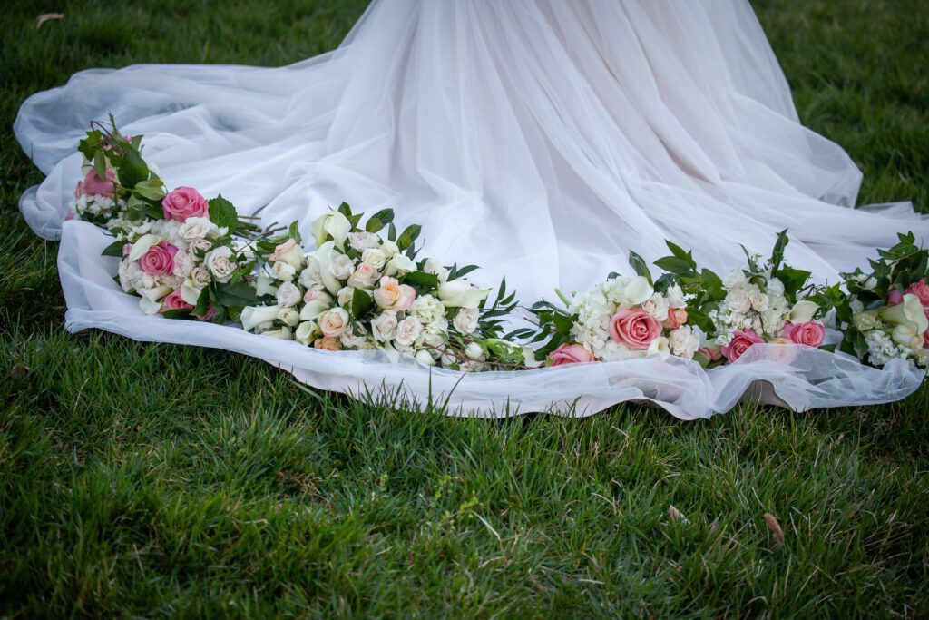 A bridal train on grass adorned with a line of elegant pink and white flowers, including roses and hydrangeas.