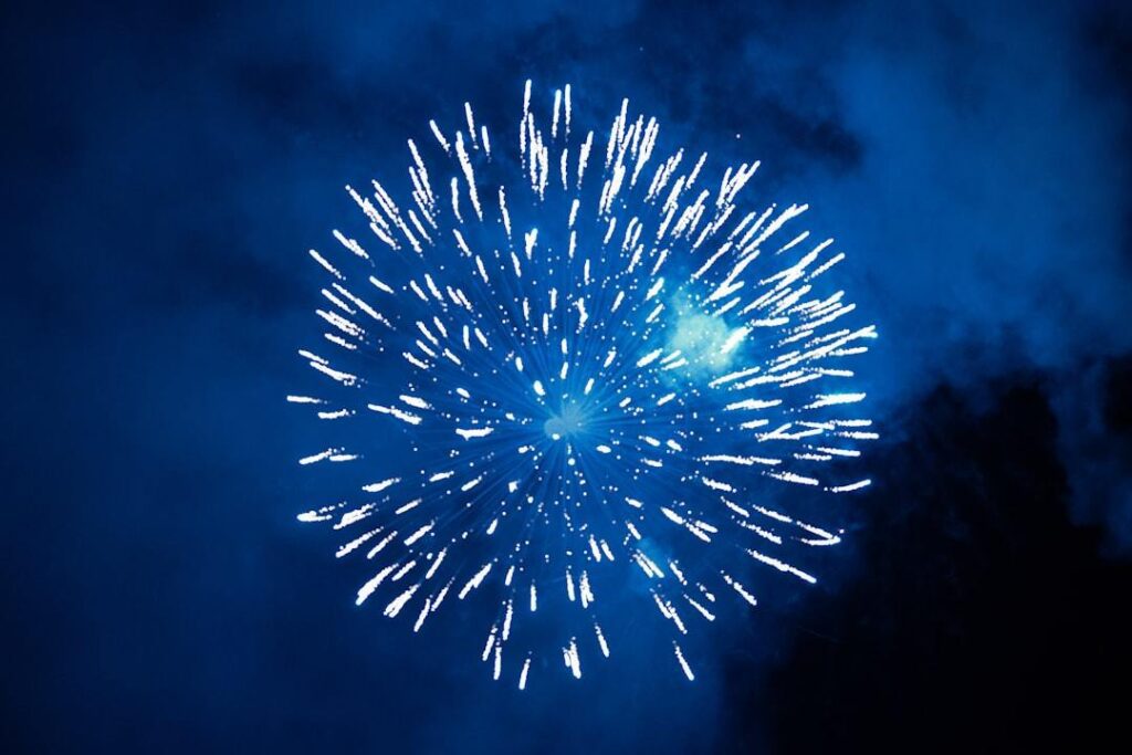 A single white firework bursts against a dark night sky, with streaks of light dispersing outward from a central point.