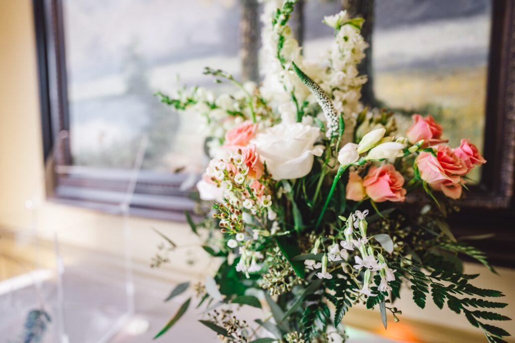 A bouquet of flowers in a vase featuring white roses, pink roses, and various white wildflowers with green foliage enhances the venue. The background is blurred, showing a framed landscape painting in a softly lit room. | Morningside Inn